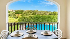Un balcon avec une table dressée pour quatre personnes, donnant sur une piscine et une végétation luxuriante.