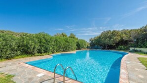Une piscine rectangulaire bordée de pierres, entourée d’une terrasse en pierre, et une échelle métallique menant à l’eau.