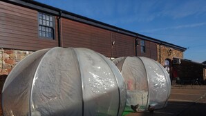 Twee grote, transparante constructies voor een gebouw met een gevel van steen en een metalen dak.
