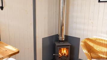 A room with a wood-burning stove, a wicker chair, and a wooden table.