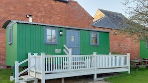 A green wooden building with a white porch and steps leading to a bench.