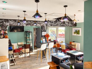 Un comedor con mesas y sillas, una zona de bar con botellas, y vistas al exterior.