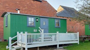 A green wooden building with a white porch and steps leading to a bench. - Ryans Retreat, shepherds hut, pet friendly close to beach and Hadrian's Wall (Bowness on Solway)
