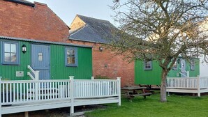 A row of green cottages with white railings and a picnic table in the foreground. - Ryans Retreat, shepherds hut, pet friendly close to beach and Hadrian's Wall (Bowness on Solway)