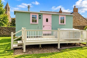 A quaint cottage with a pink door, a small porch, and a stone tower in the background.