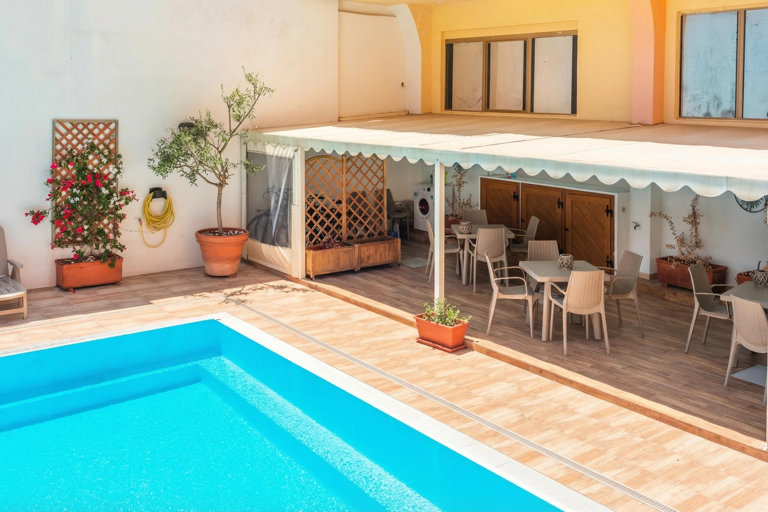 A pool area with a covered patio, potted plants, and outdoor furniture.