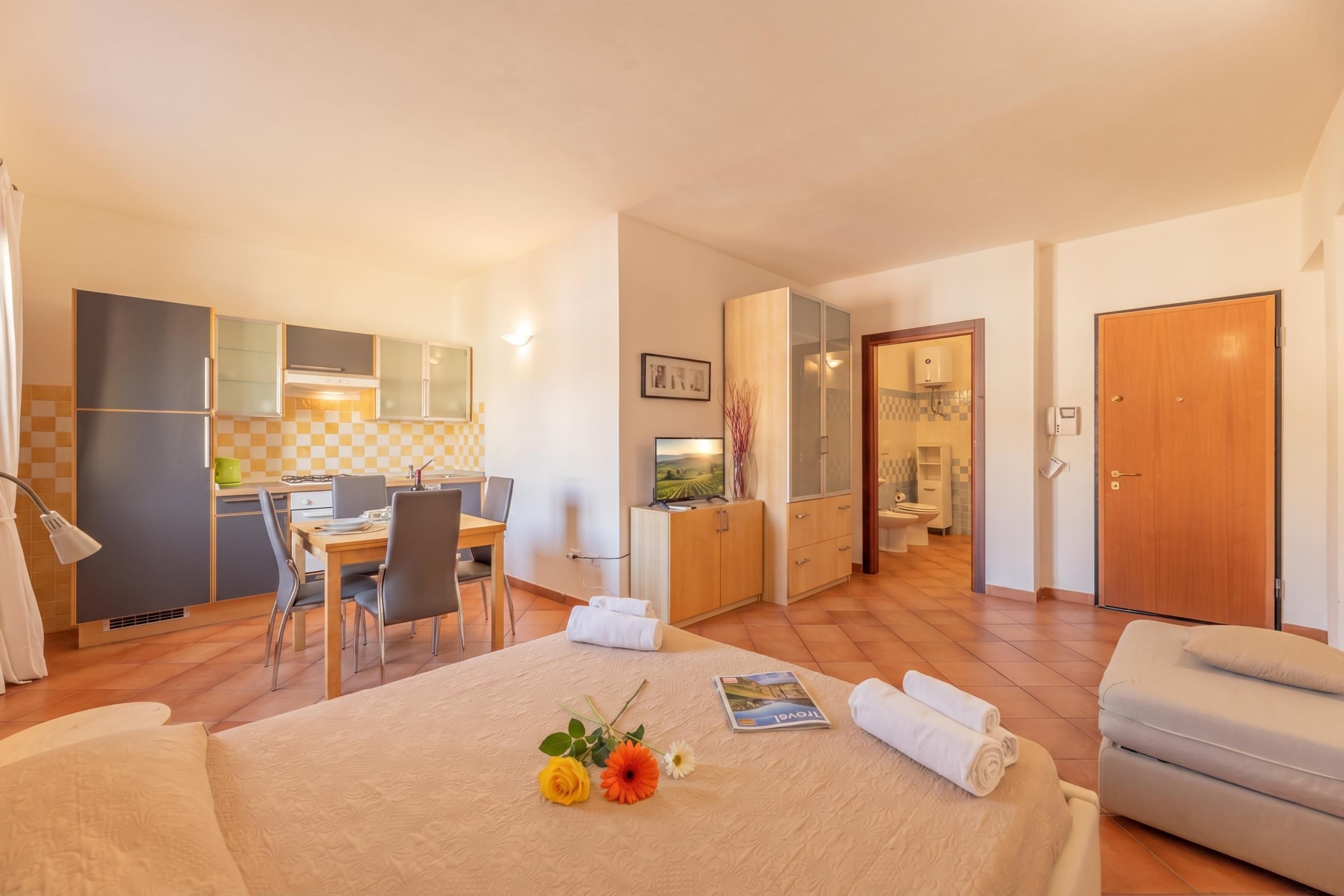 A hotel room with a bed, a desk, a chair, a kitchenette, and a bathroom.