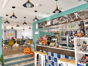 Un espace bar avec des tabourets, un comptoir où sont exposés divers articles et des luminaires suspendus.