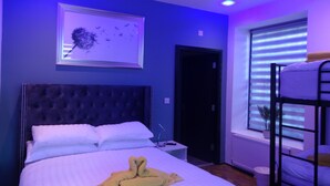 A hotel room with a large bed, a headboard, a bedside table, a framed picture on the wall, a window with blinds, and a bunk bed in the corner. - Family room in the farmhouse, breakfast included in onsite bistro close to Hadrians Wall (Bowness-on-Solway)