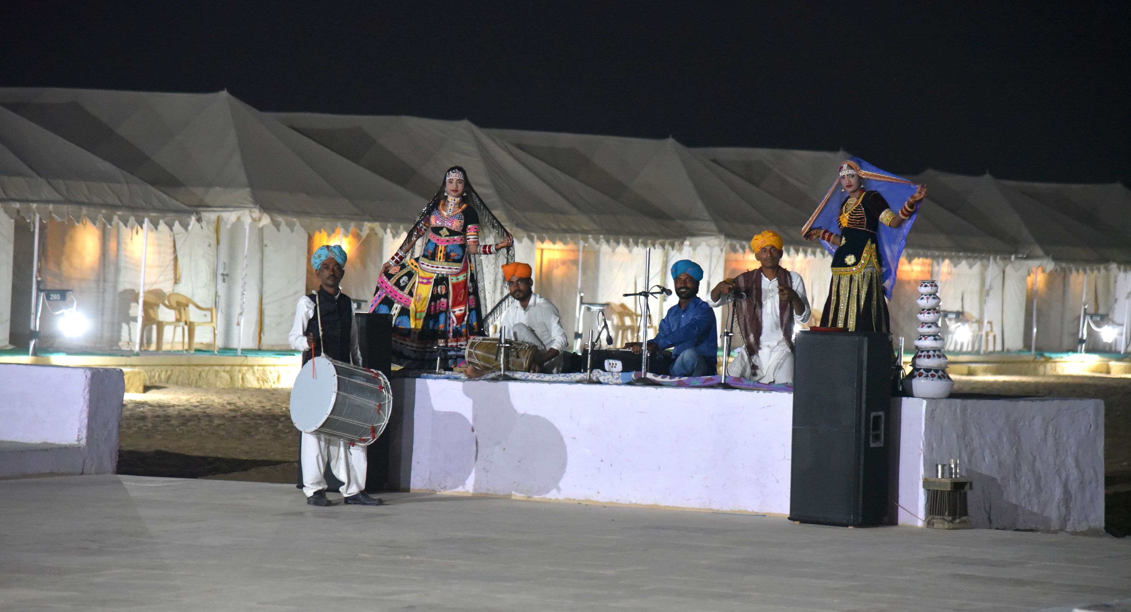 A group of musicians performing on a stage with a tent backdrop.