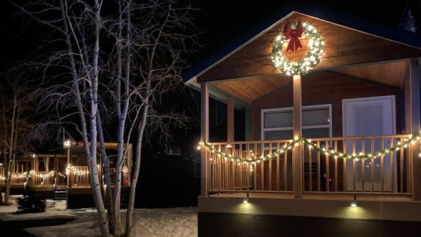 Eine Holzhütte mit Veranda, verziert mit Lichtern und einem Kranz, umgeben von Schnee.