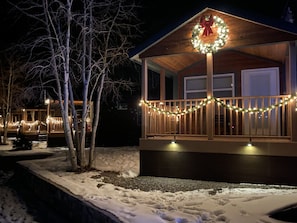 A wooden cabin with a porch decorated with lights and a wreath, surrounded by snow. - River Run Cabins (Ouray)