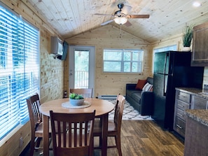 A cozy cabin interior with a wooden dining table, chairs, a ceiling fan, and a kitchen area with a refrigerator and cabinets. - River Run Cabins (Ouray)
