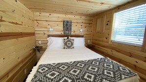 Ein Schlafzimmer einer Holzhütte mit einem Bett, einem Fenster mit Jalousien und einer Wandleuchte.