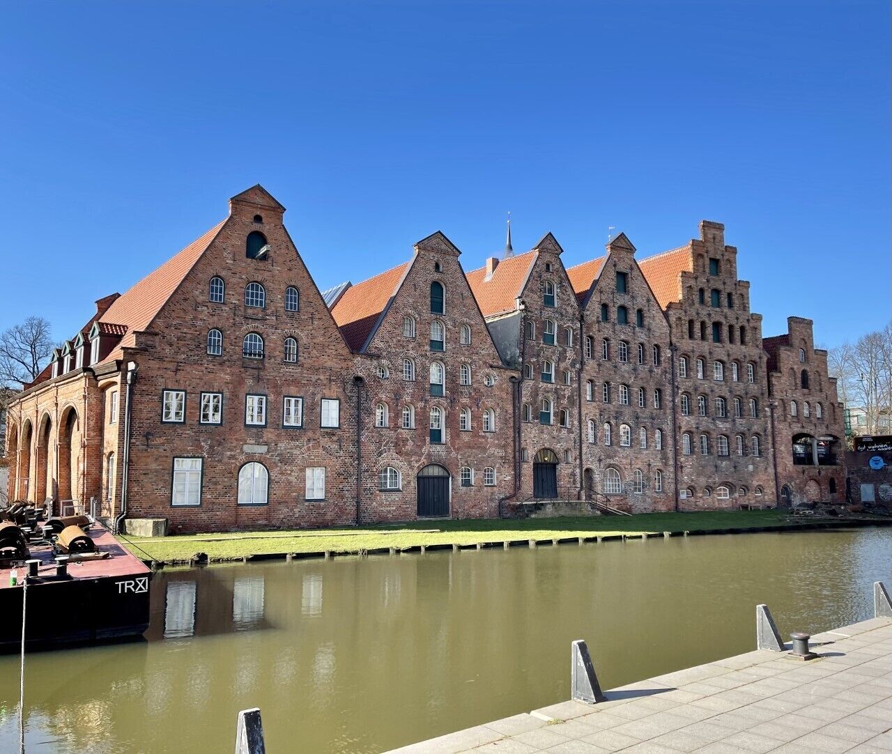 A historic brick building with multiple gabled roofs and arched windows, situated next to a calm water body.