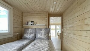 Ein Schlafzimmer einer Holzhütte mit Bett, Kissen, einem Regal mit Büchern und einem Fenster.