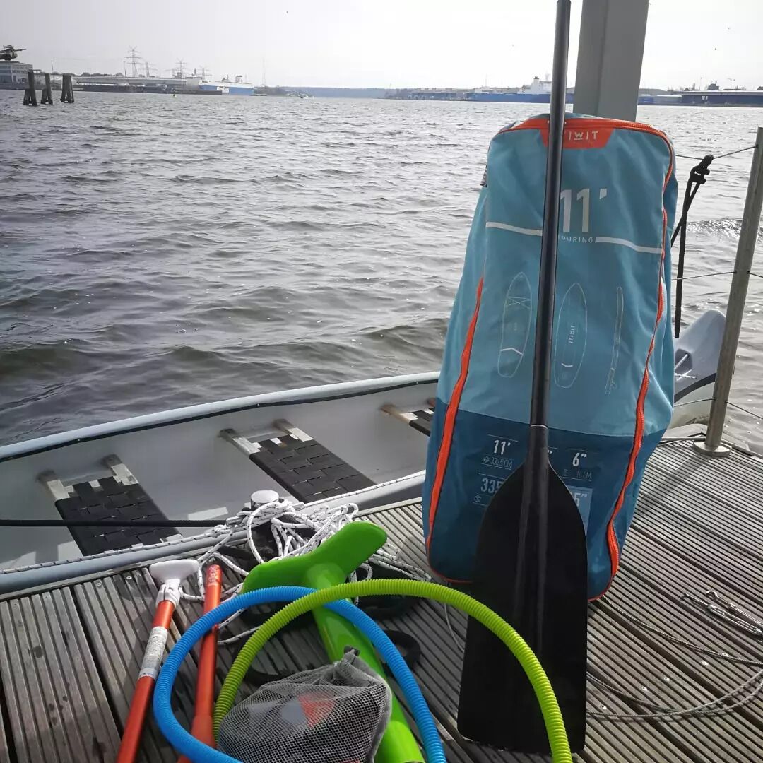 A boat deck with a blue bag labeled "11' DURING," a green and blue hose, and a black paddle.