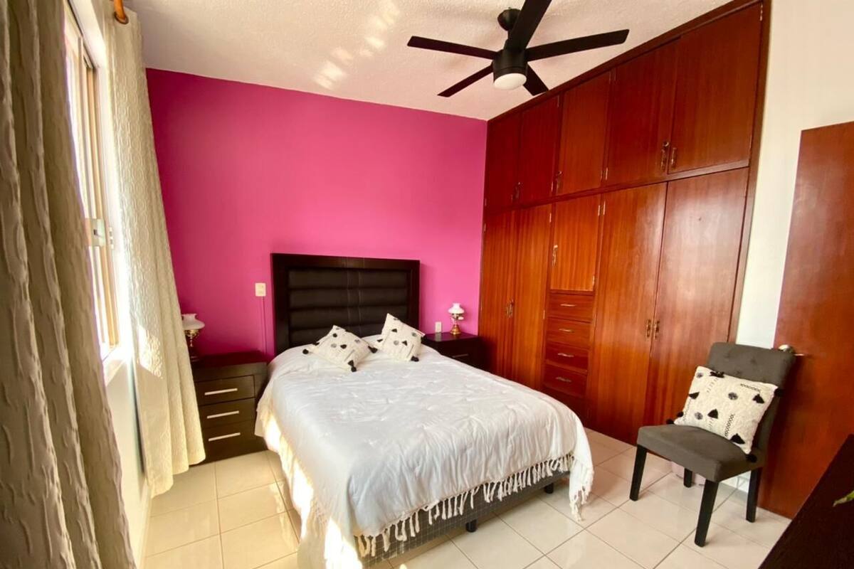 Un dormitorio con cama, una silla, armario y ventilador de techo.