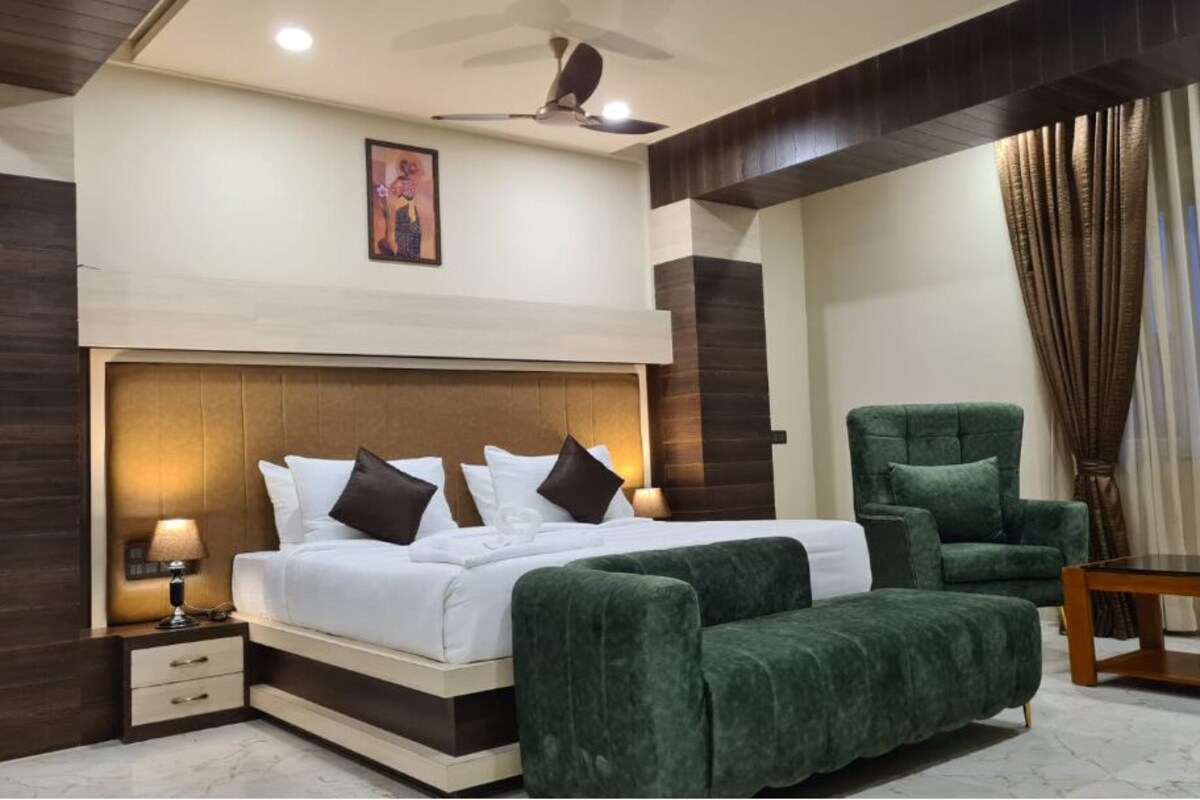 A modern bedroom with a large bed, a green armchair, a wooden coffee table, and a ceiling fan.