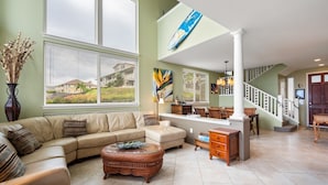 A spacious living room with a large sofa, a coffee table, and a dining area with a bench. - Alii Cove I-4 in Historic Kailua Village (Kailua Kona)