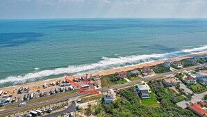 Una vista aerea di una zona costiera con spiaggia, una strada e diversi edifici, tra cui una grande casa con piscina.