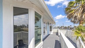 Una proprietà costiera con un balcone coperto, ampie finestre e vista sul mare e sugli edifici in lontananza.