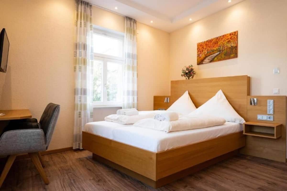 A modern hotel room with a wooden bed, a desk, and a window with curtains.