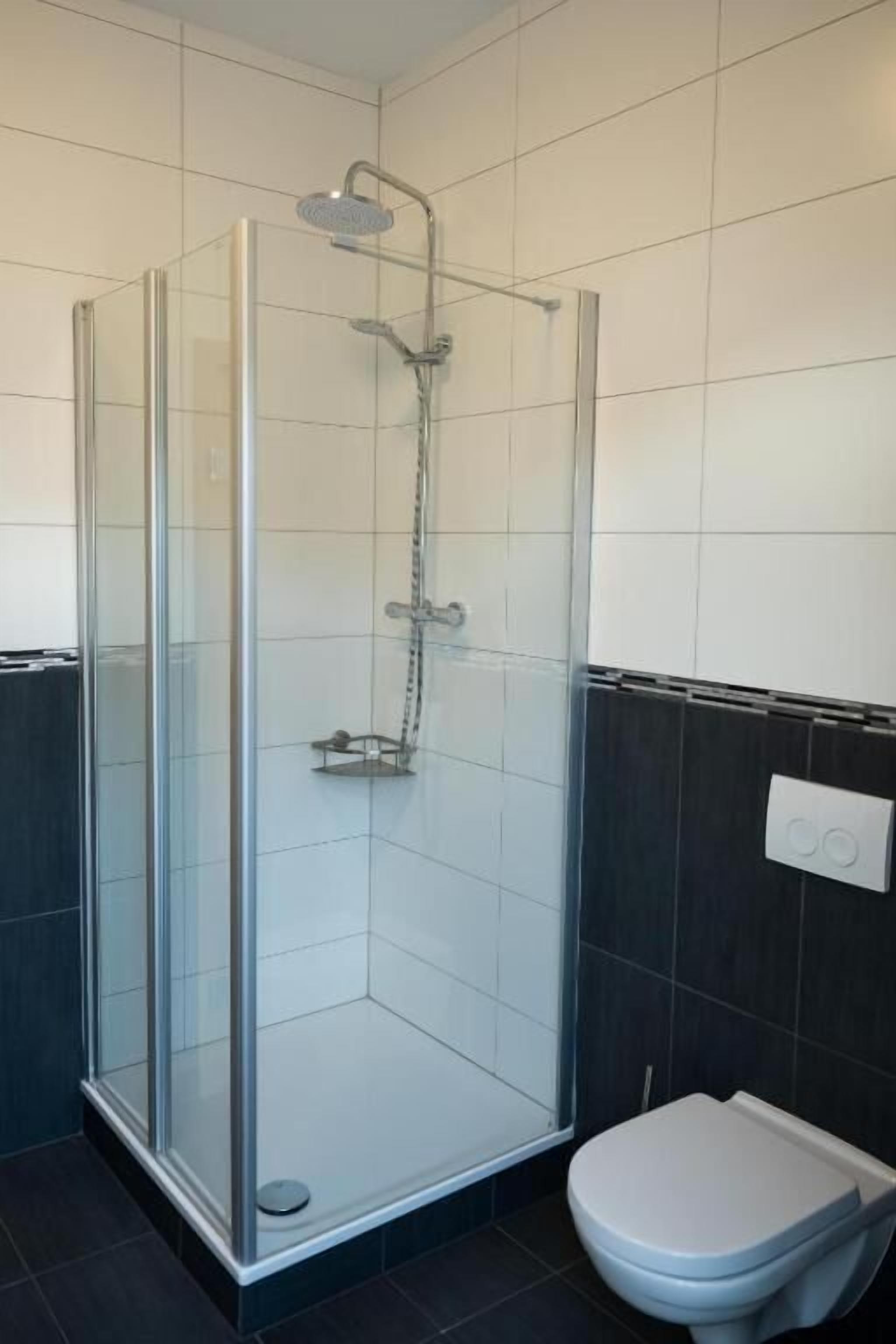 A glass-enclosed shower stall with a handheld showerhead and a wall-mounted faucet.