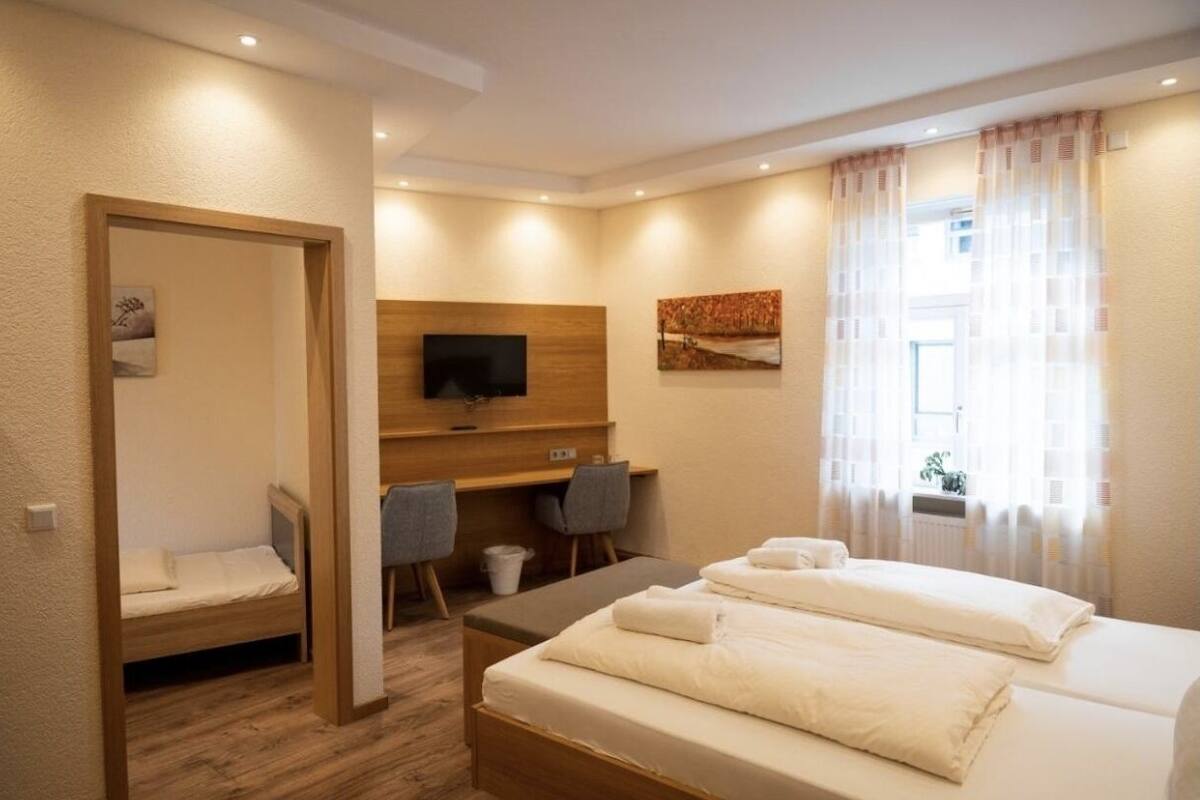 A hotel room with two beds, a desk, a TV, and a window with curtains.