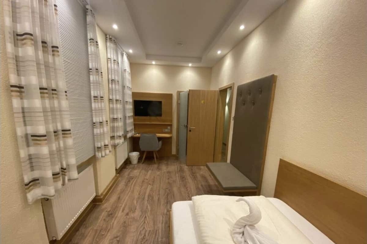 A hotel room with a bed, a desk, a chair, and a mirror.