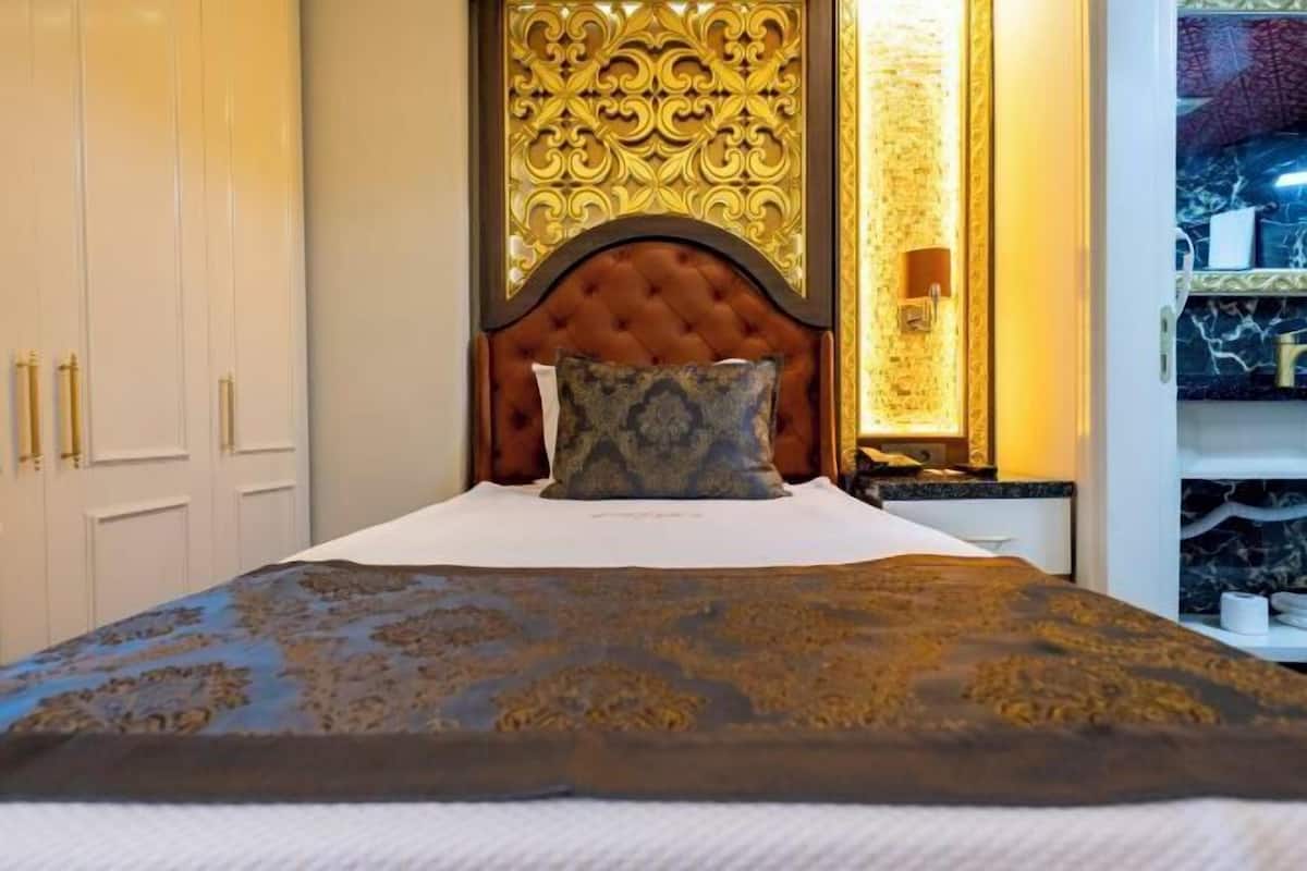 Un llit amb capçalera estofada, un edredó estampat i un panell decoratiu a la paret.