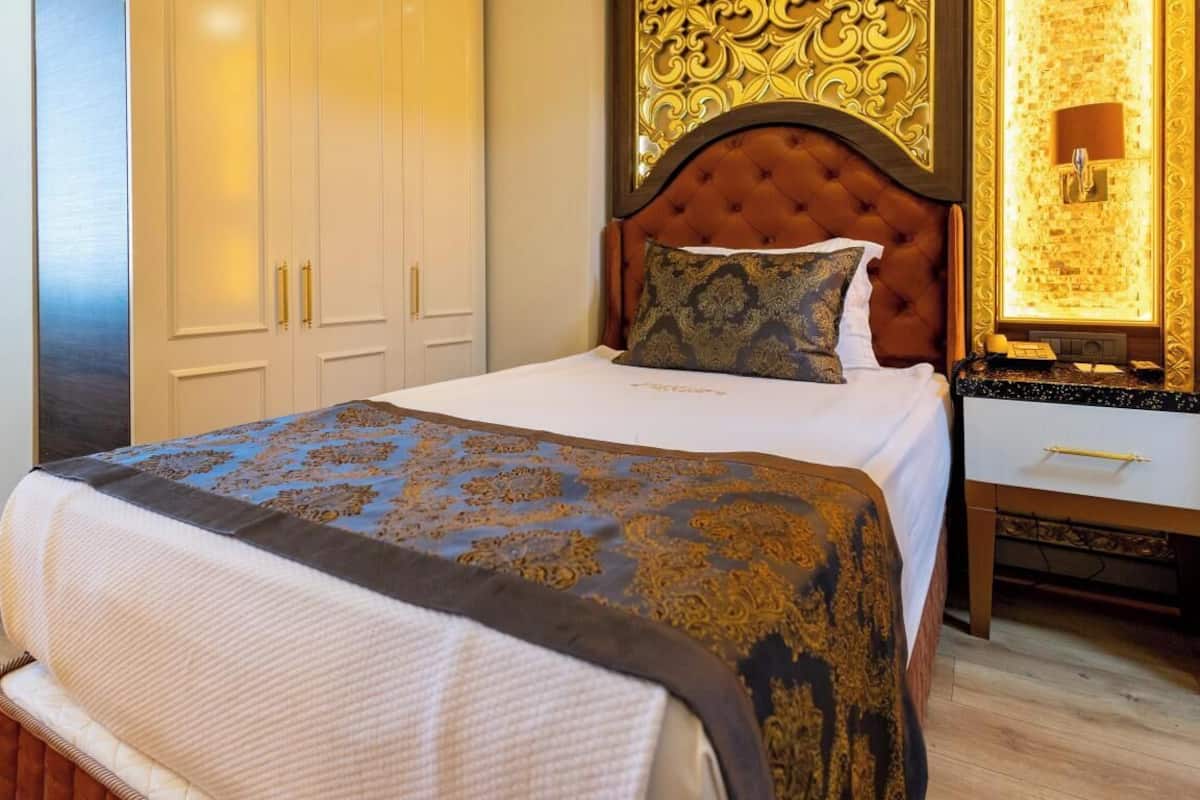 Habitació d'hotel amb un llit gran, un panell de fusta al capçal, una tauleta de nit i un armari.