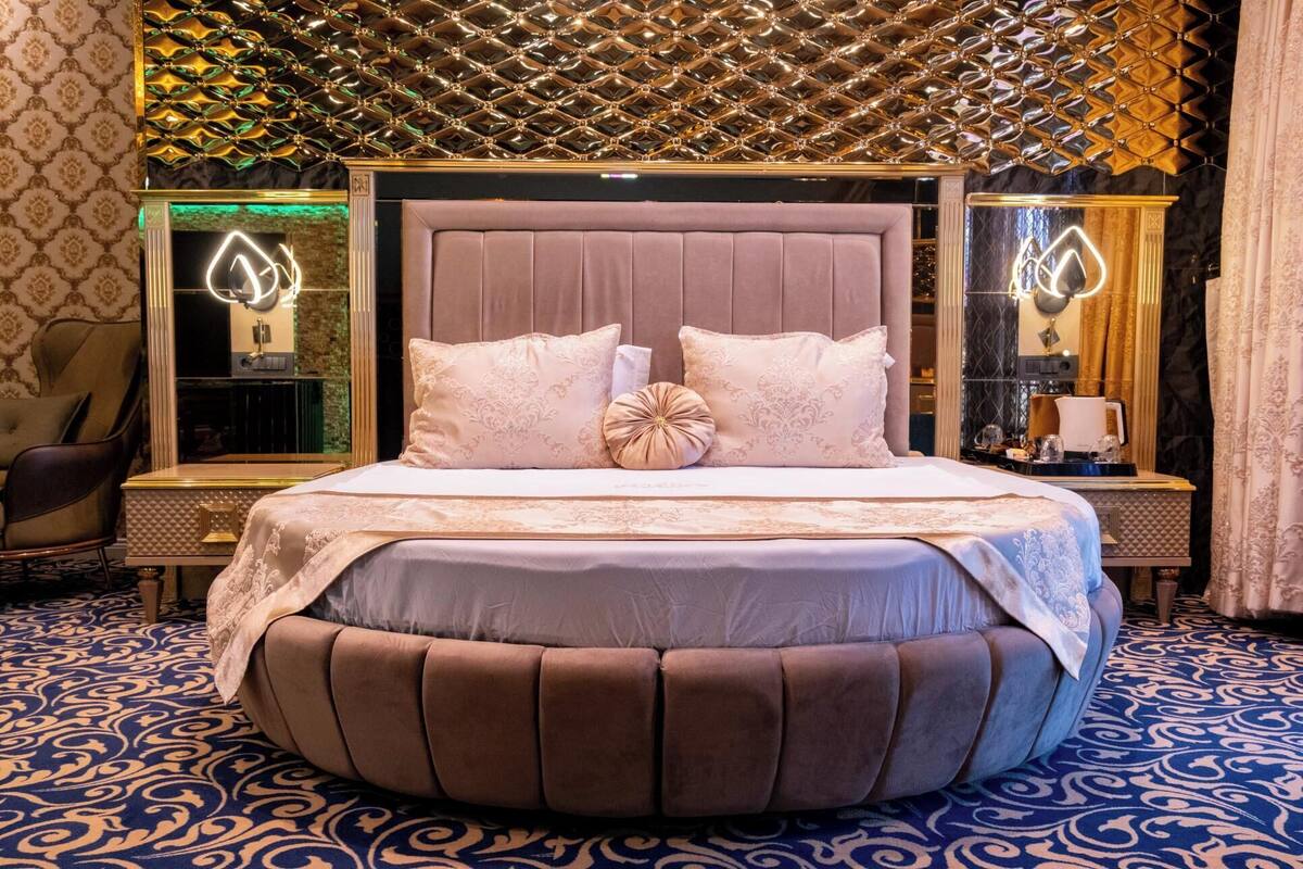 Un dormitori luxós amb un llit gran, un capçal decorat i una catifes amb dibuixos.