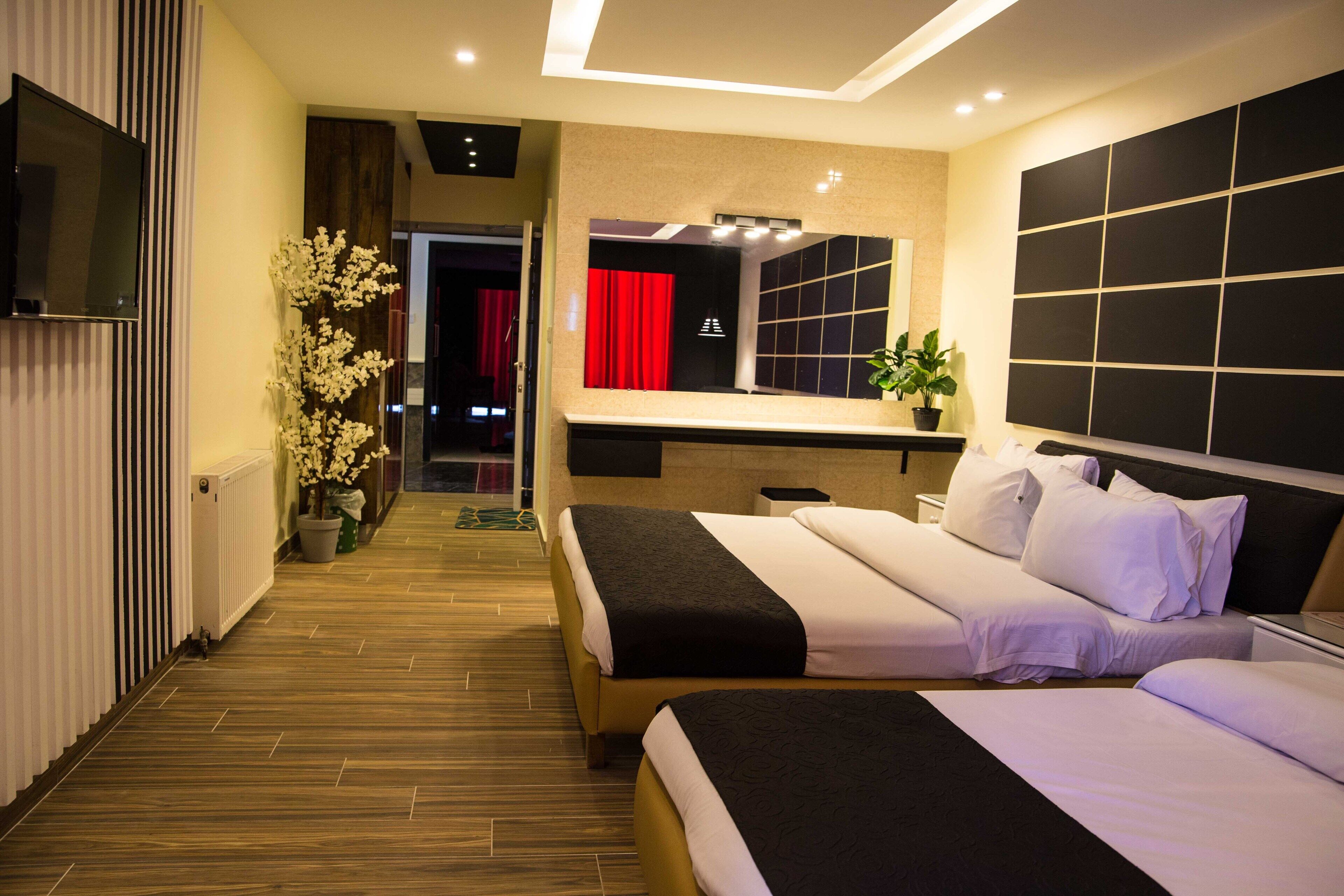 A hotel room with two beds, a TV, a mirror, and a potted plant.