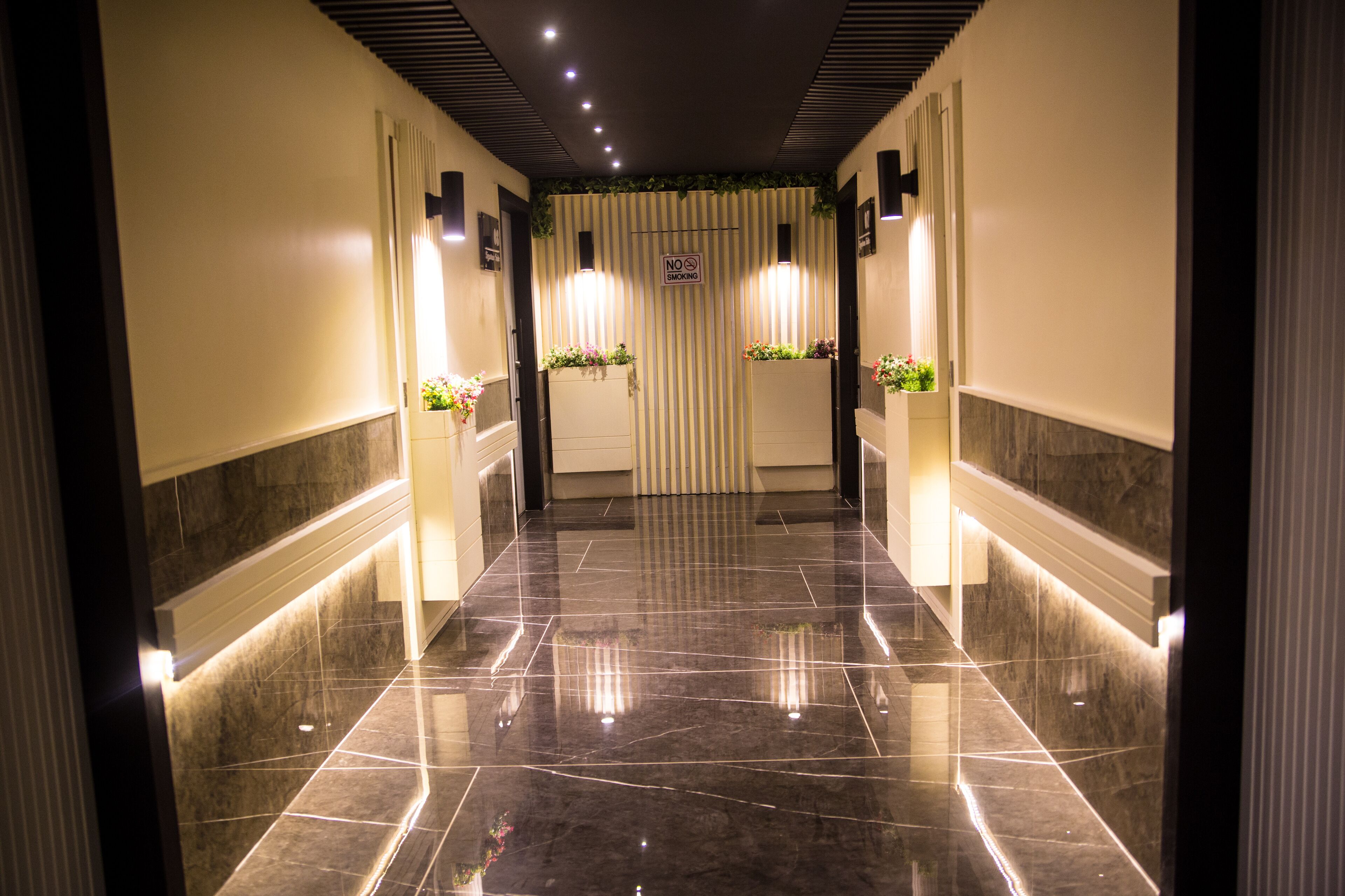 A polished hallway with a 'No Smoking' sign, decorative plants, and a modern ceiling design.