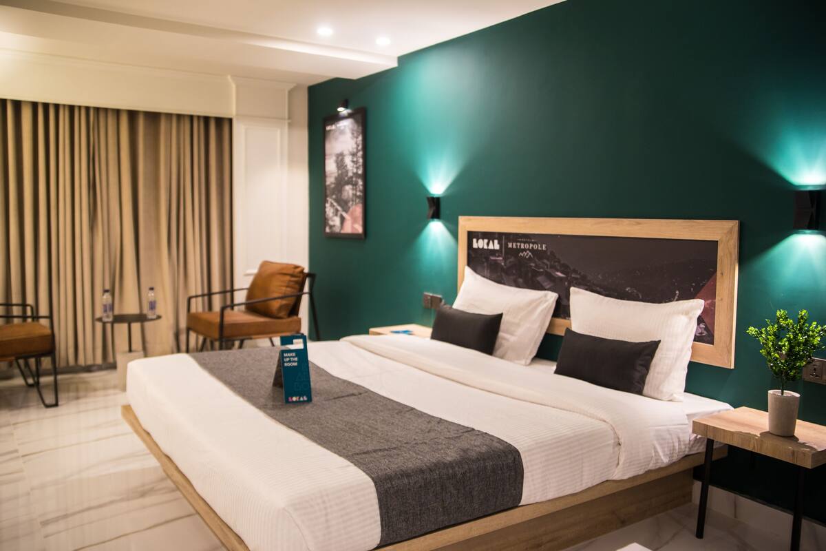 A modern hotel room with a large bed, a desk, a chair, and a potted plant.
