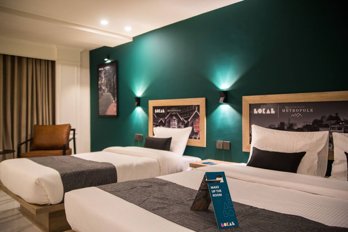 A hotel room with two beds, a brown leather chair, and wall-mounted lights.