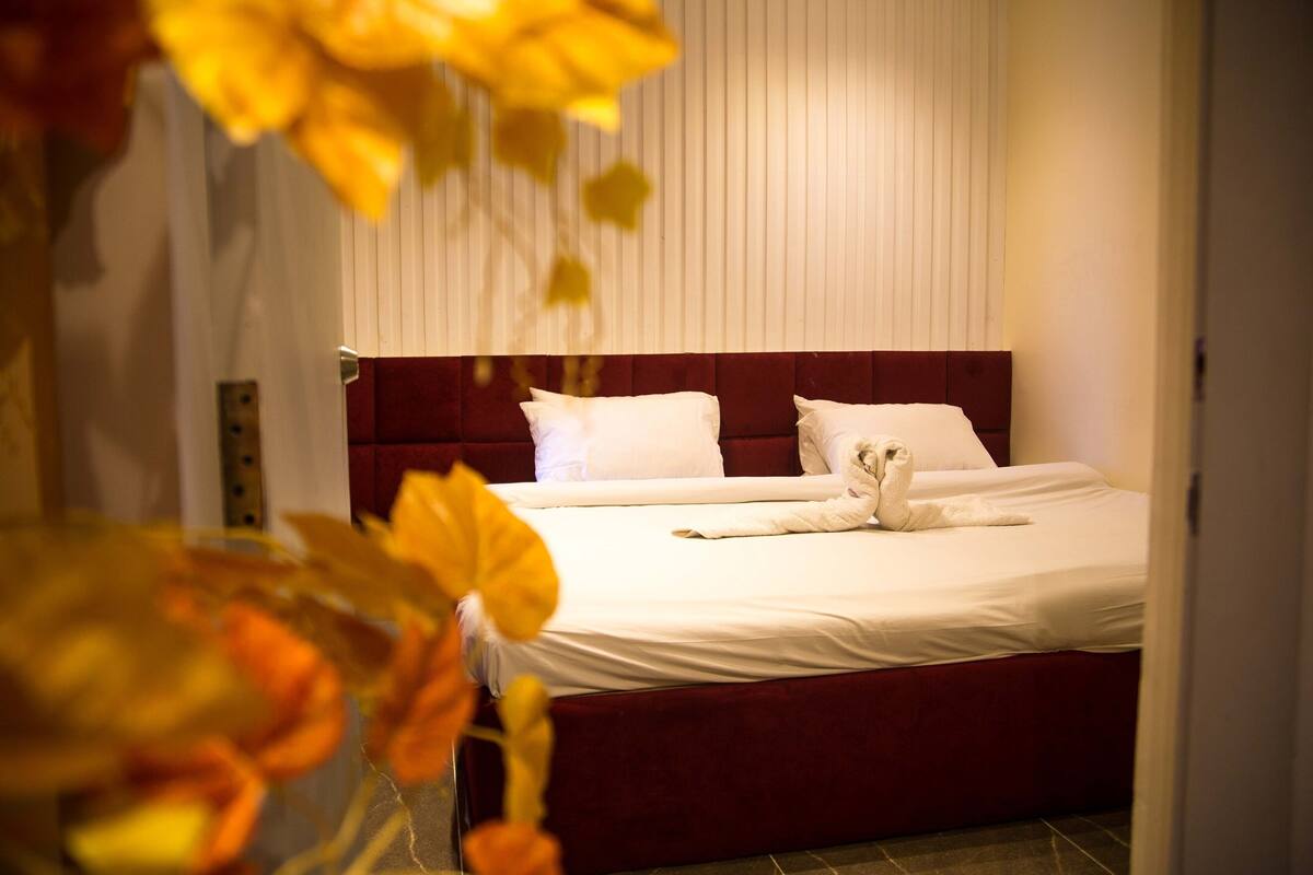 A neatly made bed with white linens and a red headboard in a hotel room.