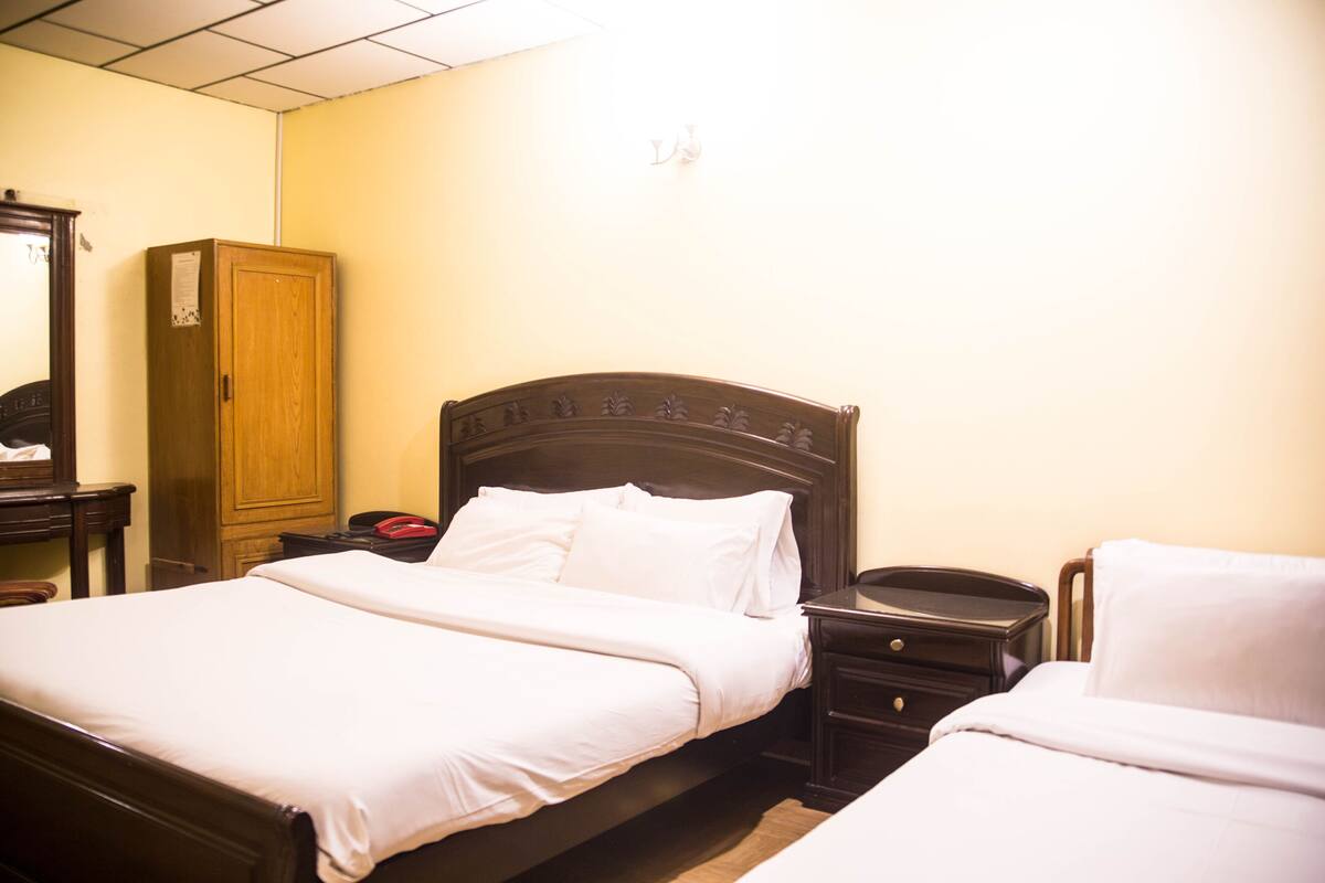 A hotel room with two single beds, wooden headboards, a wooden wardrobe, and a bedside table with a telephone.