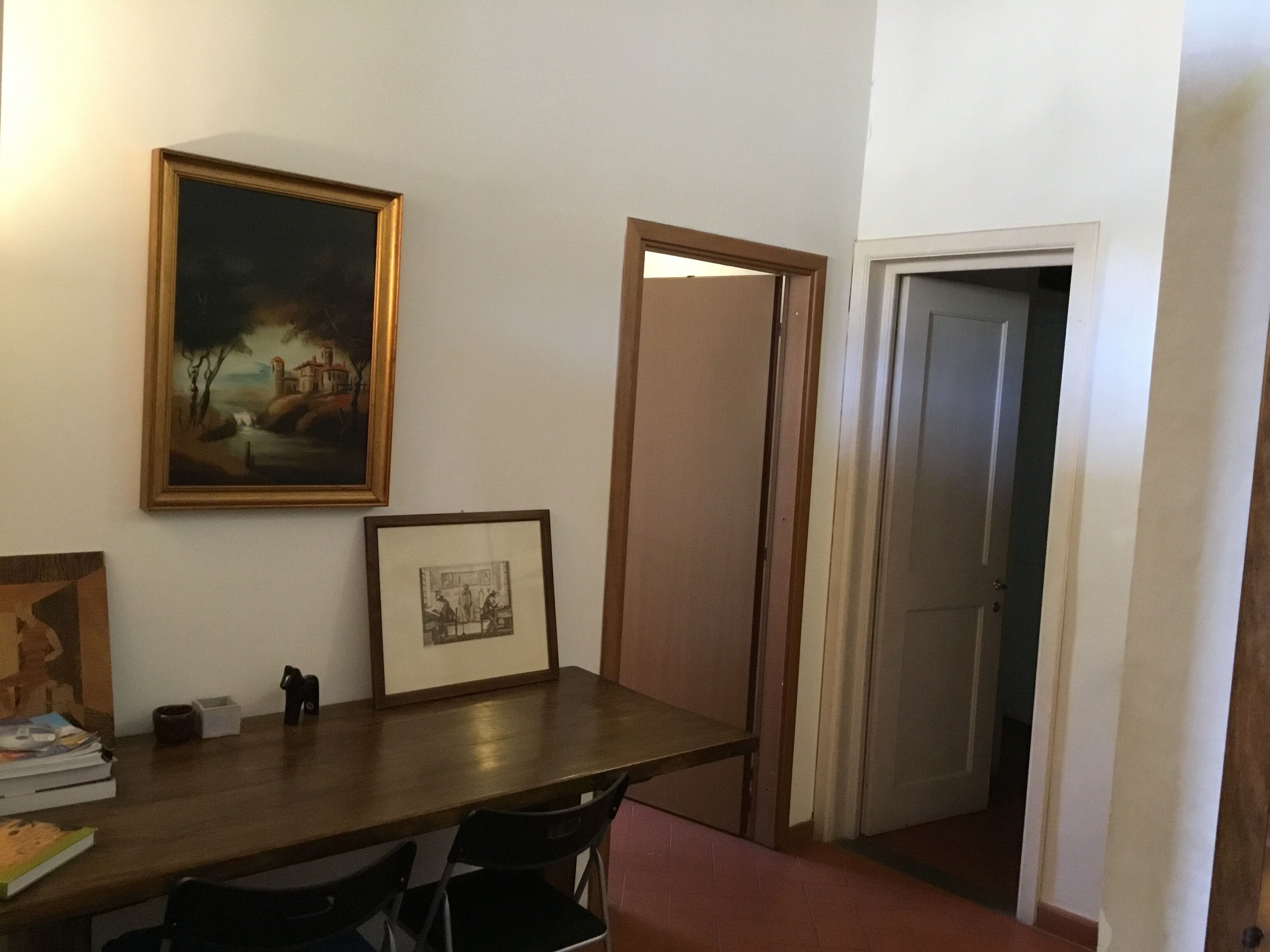 A room with a wooden table, two chairs, a framed picture, and a door leading to another room.