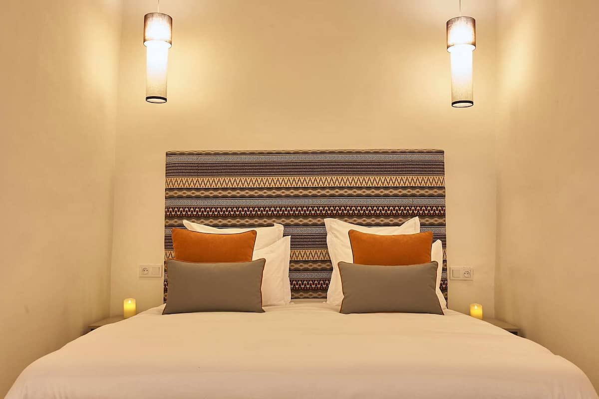 A hotel room with a patterned headboard, two bedside lamps, and a bed with pillows.