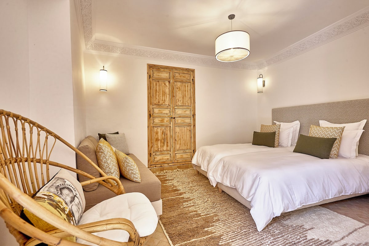 A bedroom with a bed, a sofa, a chair, and a wooden door.