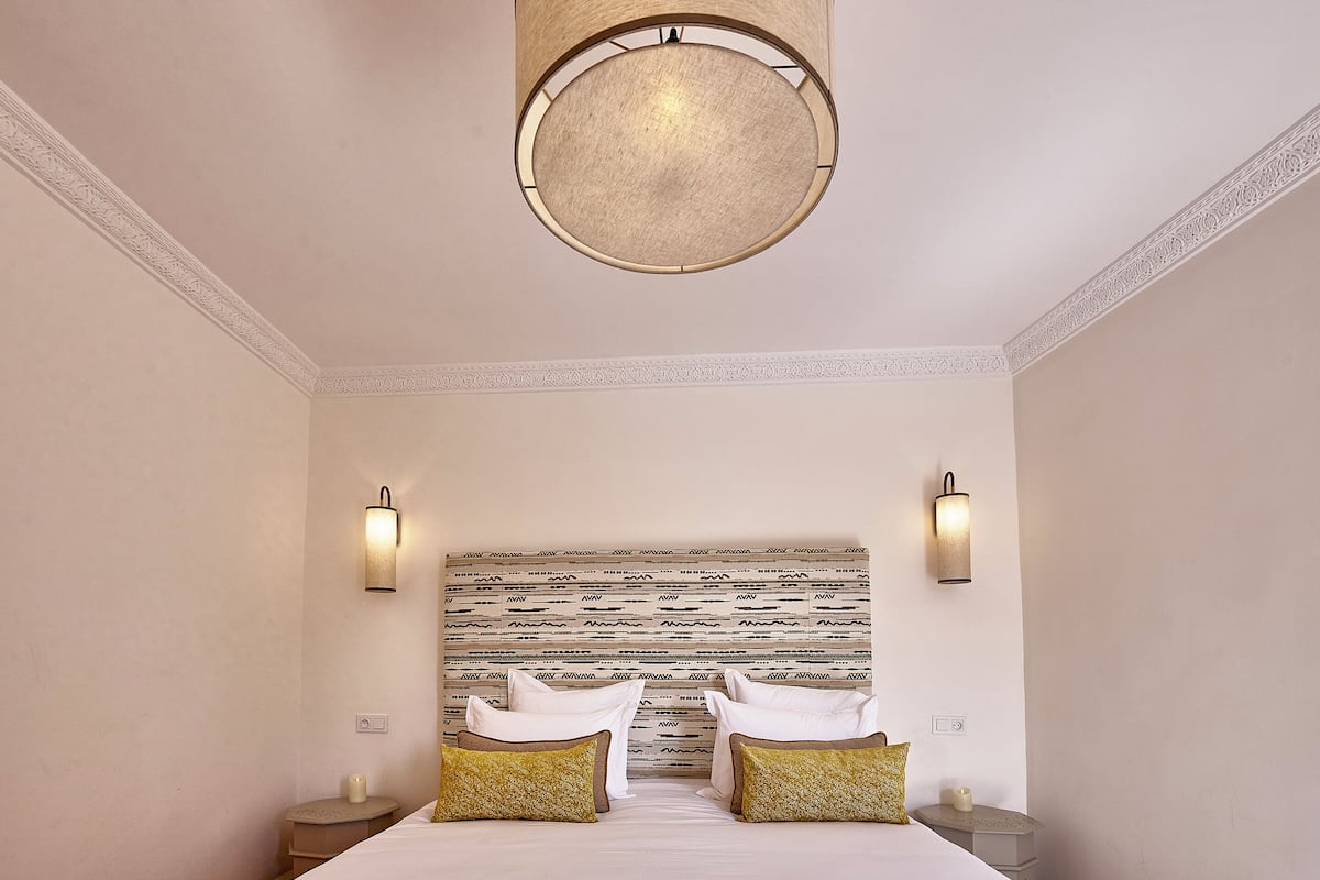 A hotel room with a large bed, two bedside tables, a round ceiling light, and a patterned headboard.