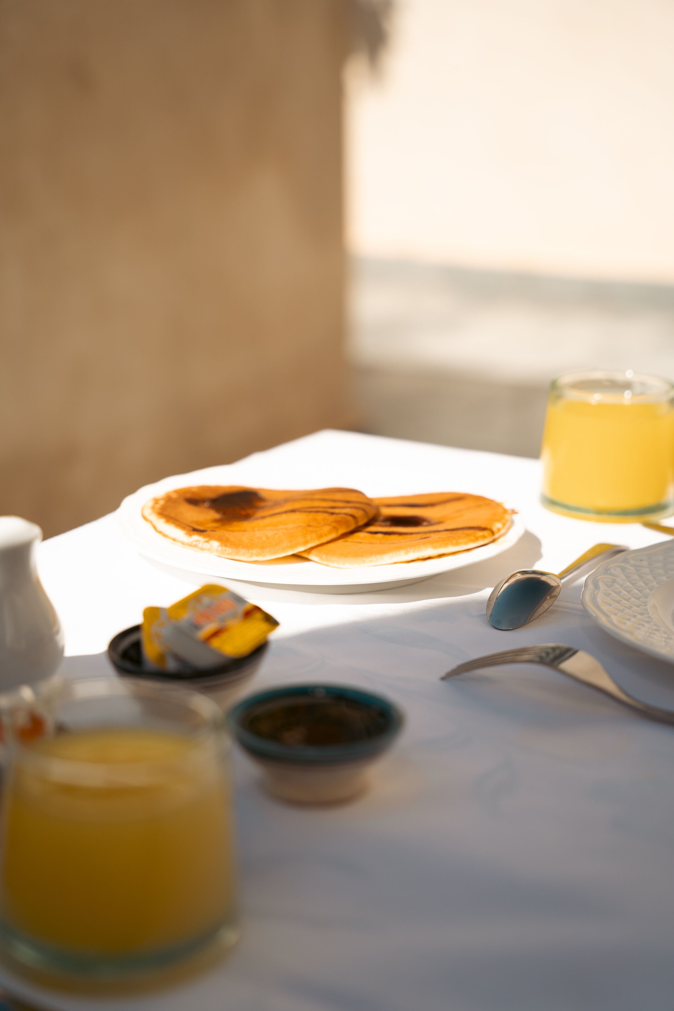 A breakfast table with pancakes, a glass of orange juice, and a small bowl of jam.