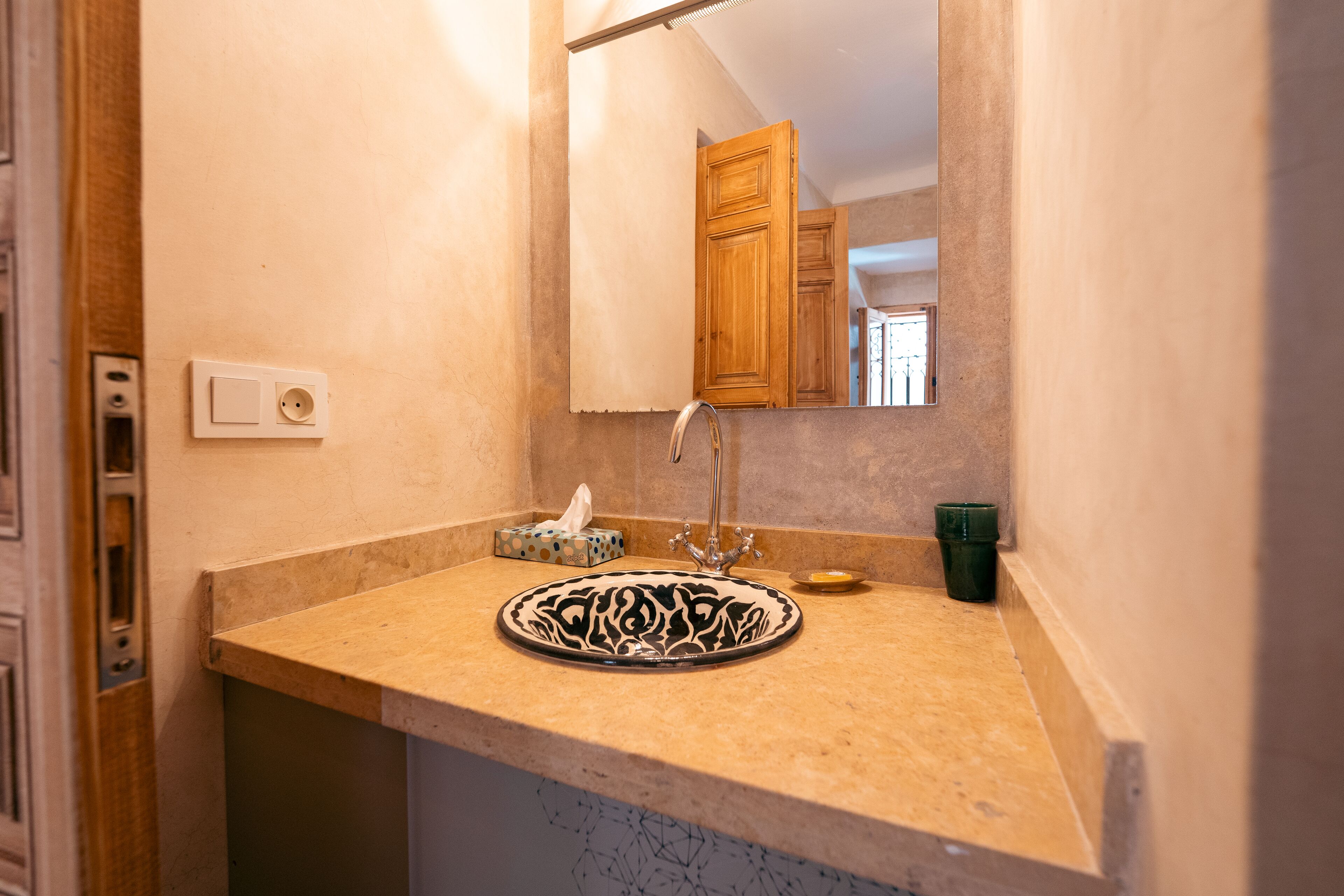 A bathroom with a beige countertop, a sink with a decorative basin, a mirror, and wooden cabinets.