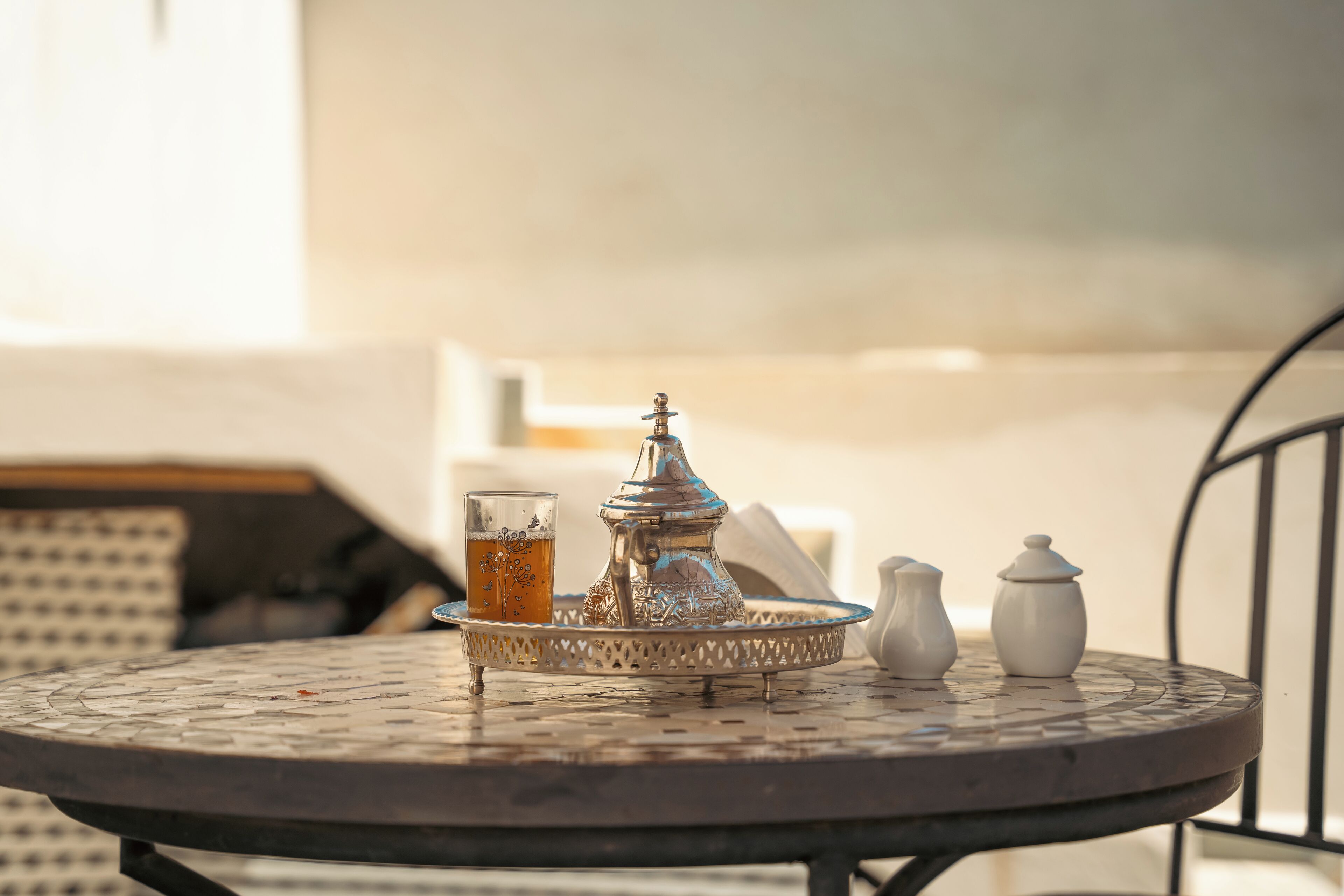A round metal table with a Moroccan tea set, including a teapot, cups, and sugar bowls.