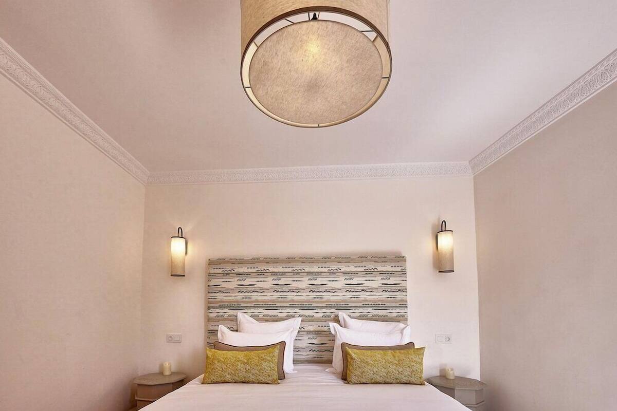 A hotel room with a bed, two bedside tables, a round ceiling light, and a patterned headboard.