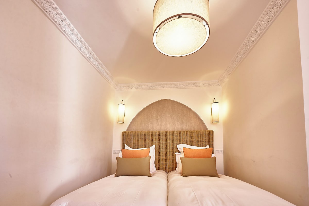 A double bed with two pillows, a headboard with a textured pattern, and two wall-mounted lights.