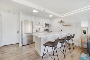 Uma cozinha moderna com armários brancos, eletrodomésticos de aço inoxidável e uma ilha central com banquetas.