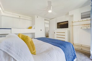 Quarto com cama, ventoinha no teto, televisão, guarda-roupa e cabideiro.